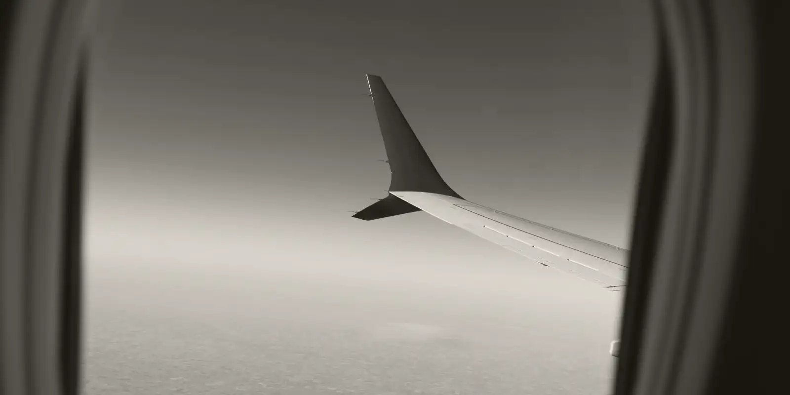 An aircraft wing seen from a cabin window above the clouds.